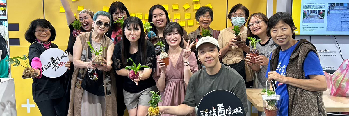 可及協會在環境不要障礙的活動時的團體照，總共12位成員，每個人帶著笑容並拿著綠色盆栽一起提倡環境不要障礙。